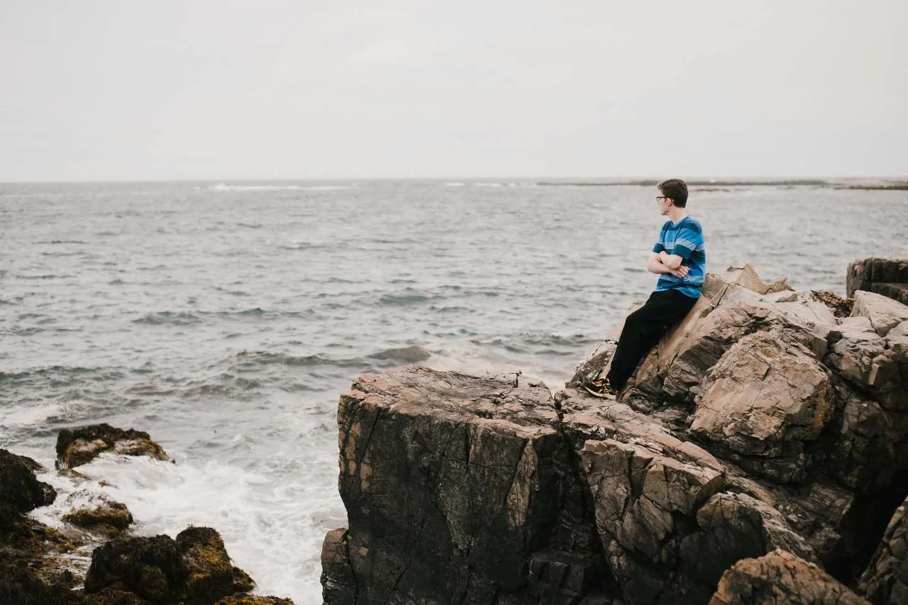 man leaning against a rock on the shore in Maine